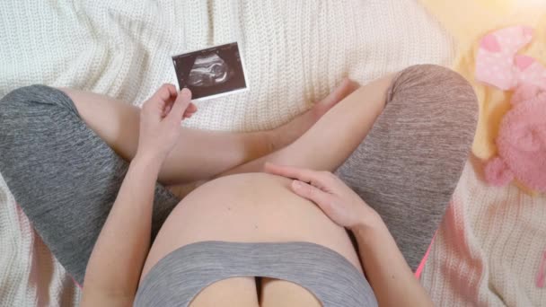 Pregnant woman holding ultrasound image. Concept of pregnancy. Top view - Filmagem, Vídeo