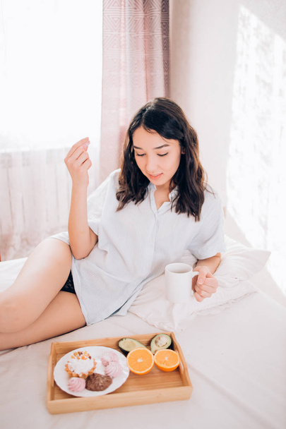 Young woman eating healthy breakfast in bed - Fotoğraf, Görsel