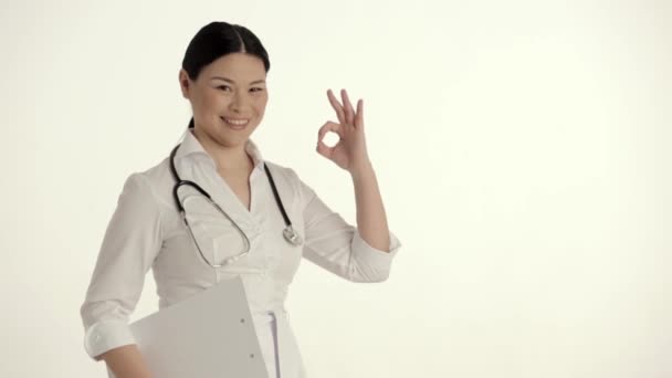 Asian Nurse on White Background Smiles and Lifts Thumb. - Filmati, video