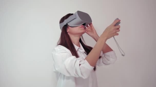 Young woman in VR headset looks around and wonders how amazing. Virtual reality helmet on white background - Video, Çekim
