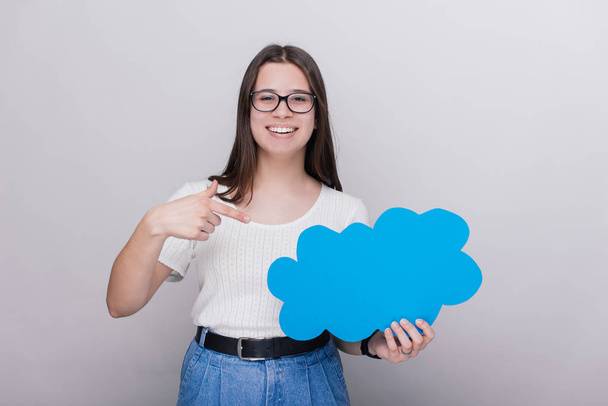 Portrait of a happy young girl pointing at blank speech bubble isolated over gray background - Photo, Image