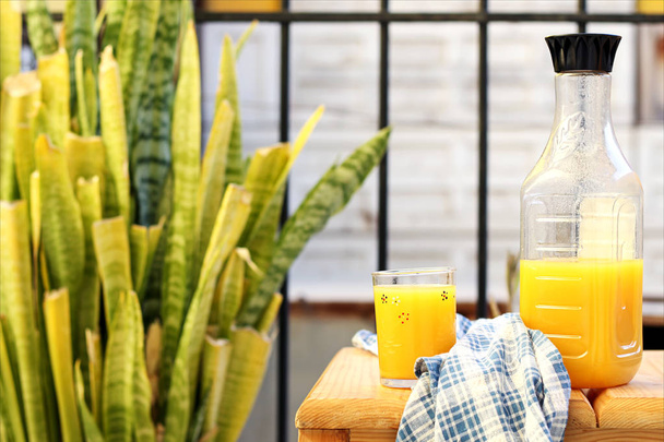 Bouteille en plastique de jus d'orange frais et tasse en verre sur table en bois à l'extérieur dans le jardin
 - Photo, image