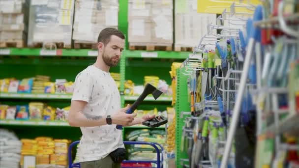 Volwassen man is het nemen van bijl in een winkel zaal, inspecteren en zetten terug op rack - Video