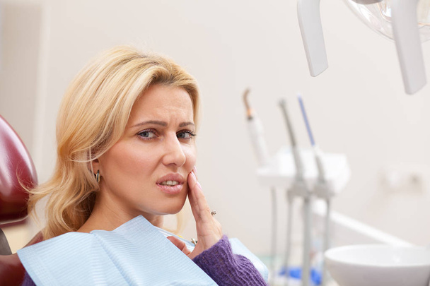 Lähikuva kaunis kypsä nainen näyttää uupunut kärsimystä hammassärky, kopioi tilaa. Naispotilas, jolla on kivuliaita hampaita, katsoo kameraan odottaessaan hammaslääkäriä
  - Valokuva, kuva