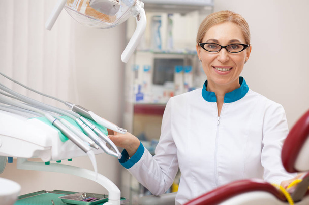Happy mature female dentist at work. Cheerful professional dentist adjusting dental lam, preparing for dental examination with patient, copy space. Professionalism, experience concept - Photo, Image