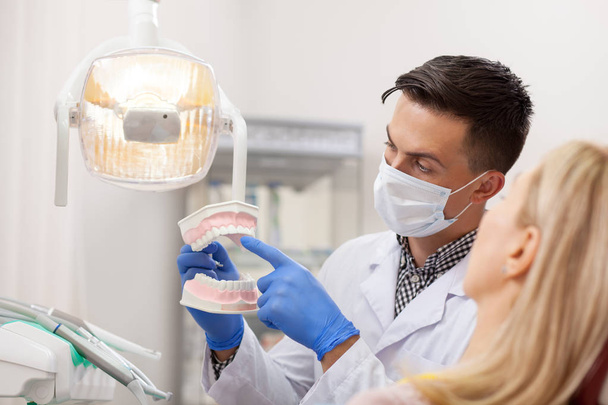 Male dentist explaining his female patient about teeth care, showing her dental mold. Professional dentist working at his office. Woman visiting dentist for oral checkup. Communication, treatment - Foto, Imagen