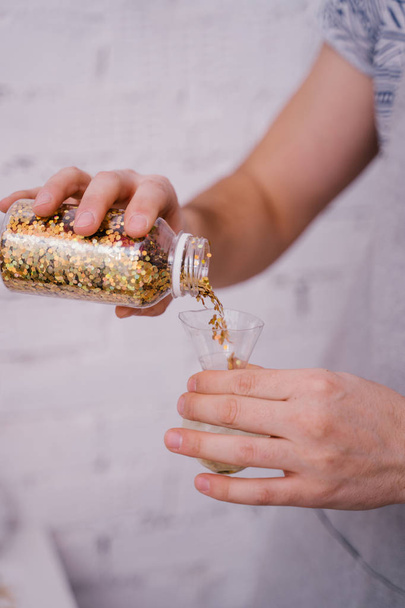 mani femminili versando coriandoli d'oro decorativi da bottiglia in pacco, primo piano
 - Foto, immagini