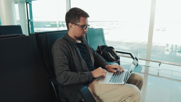 Alone serious man is surfing internet on laptop using free wifi in airport hall - Footage, Video
