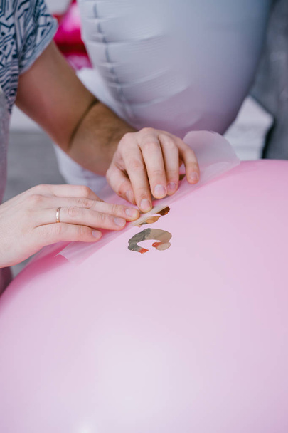 γυναικεία χέρια κολλώντας διακοσμητικά χρυσά γράμματα στην επιφάνεια του ροζ μπαλόνι, κοντινό-up   - Φωτογραφία, εικόνα