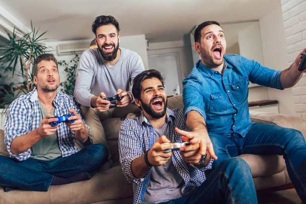 Lachende mannelijke vrienden spelen videospelletjes thuis en hebben plezier. - Foto, afbeelding