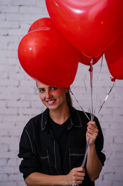 молода жінка тримає червоні серцеві кульки і позує на цегляному фоні студії, концепція вечірки на день народження
  - Фото, зображення