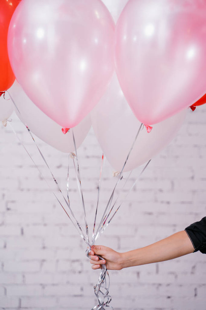 female hand holding colorful balloons on brick wall studio background , birthday concept  - Foto, Imagen
