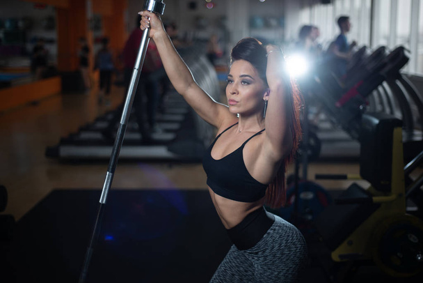 Girl posing in the gym, showing off her body, holding a barbell - Φωτογραφία, εικόνα