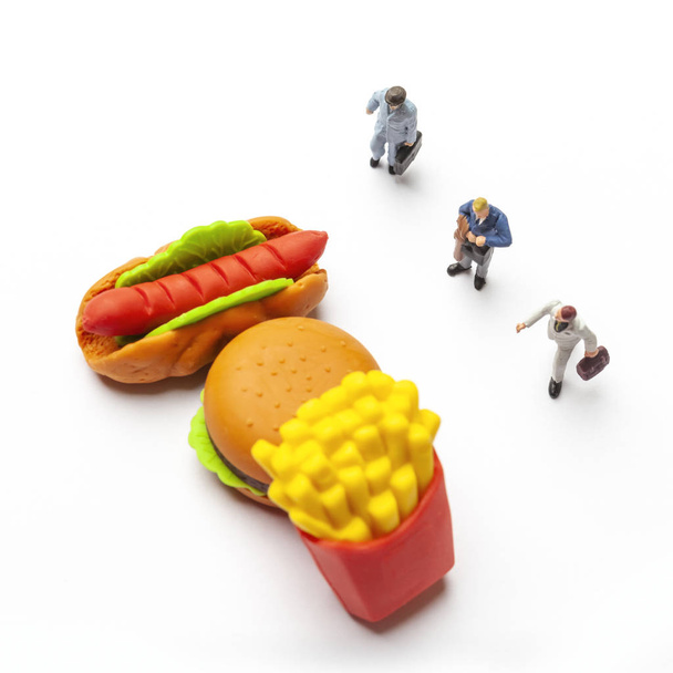 Ongezond eten concept met verliezen van miniatuur mensen en fastfood. - Foto, afbeelding