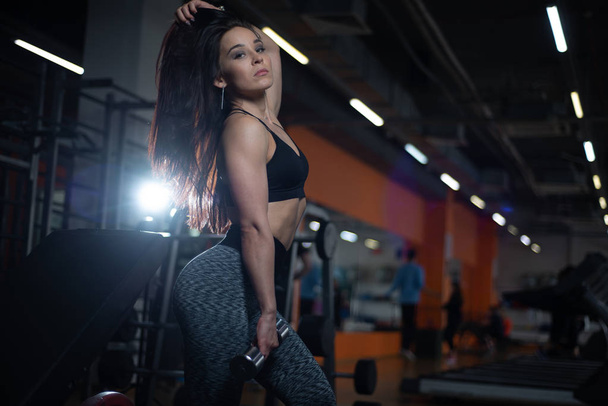 Fitness girl trains biceps with dumbbells in the gym. - Foto, Imagen