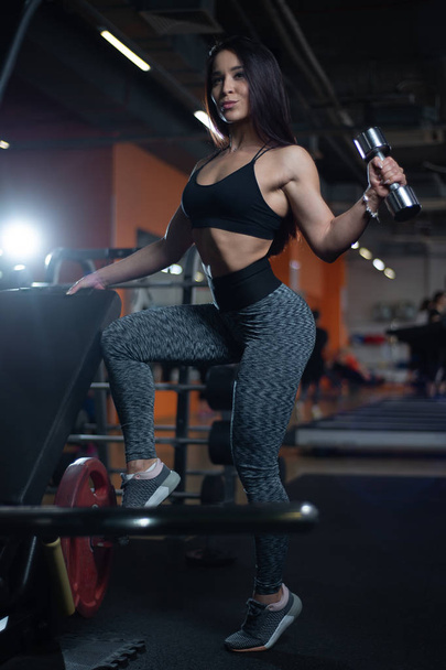 Fitness girl trains biceps with dumbbells in the gym. - Photo, Image