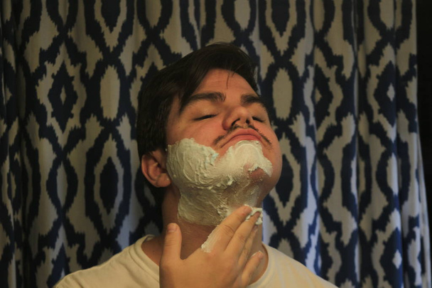 Mann zwischen 18 und 25 Jahren rasiert sich im Spiegel - Foto, Bild