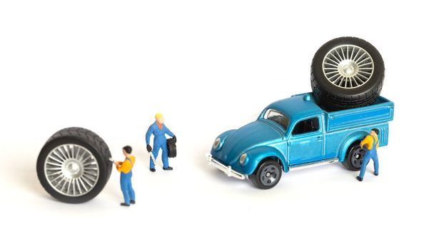 Концепция мастерской шиномонтажа. Миниатюрные механики ремонтируют пыльное игрушечное колесо автомобиля, крупным планом
. - Фото, изображение