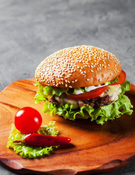burger with meat, cheese and vegetables on wooden board - Фото, изображение
