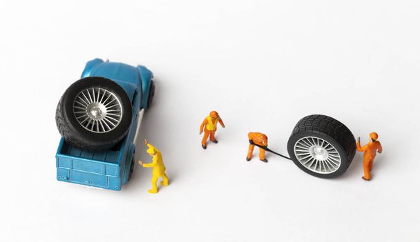 das Konzept der Werkstattreifenmontage. Miniaturmechaniker reparieren staubiges Spielzeugauto-Rad aus nächster Nähe. - Foto, Bild