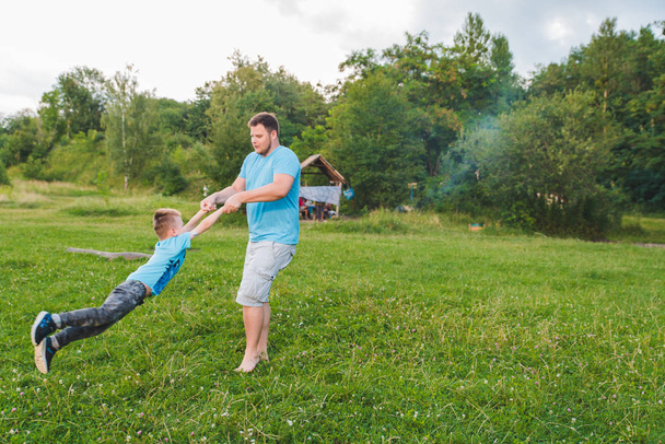 man spinning boy at green field. playing around - Photo, Image