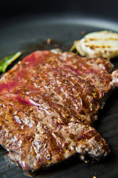 Rundvlees flank steak in de pan. Donkere achtergrond, zijaanzicht, selecti - Foto, afbeelding
