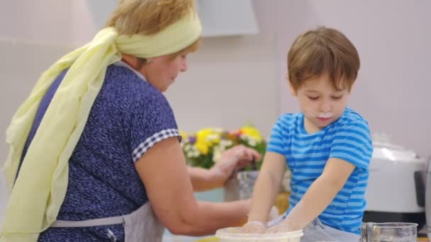 Close up of the happy smiled grandmother and grandson kneading a daugh together. slow motion of an elderly woman and little boy preparing pasta or pizza together. - Footage, Video