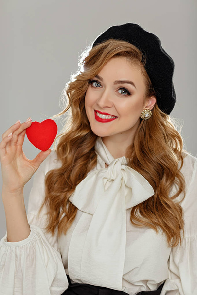 A very beautiful girl with red lips holds a red heart in her han - Fotó, kép
