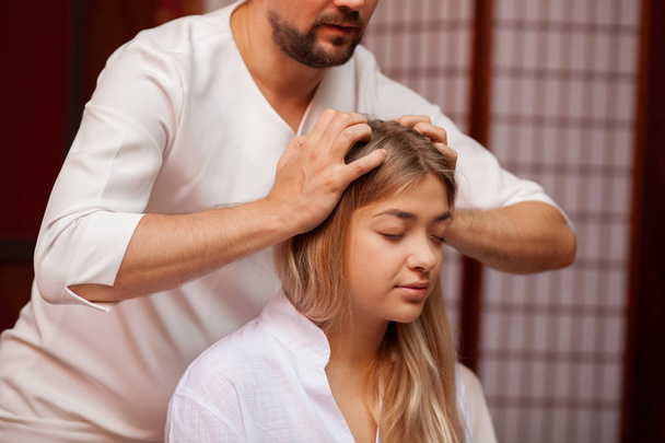 Beautiful serene woman smiling joyfully, while professional thai masseur massaging her head. Attractive woman receiving head massage at thai spa center. Stress relief, healing, health concept - Photo, Image