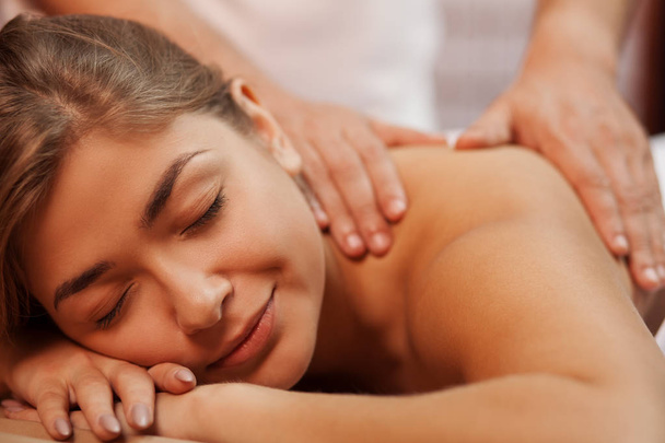 Cropped close up of a beautiful happy healthy young woman smiling with her eyes closed, while professional masseur massaging her back and shoulder, copy space. Medical treatment, stress relief concept - Foto, Imagem