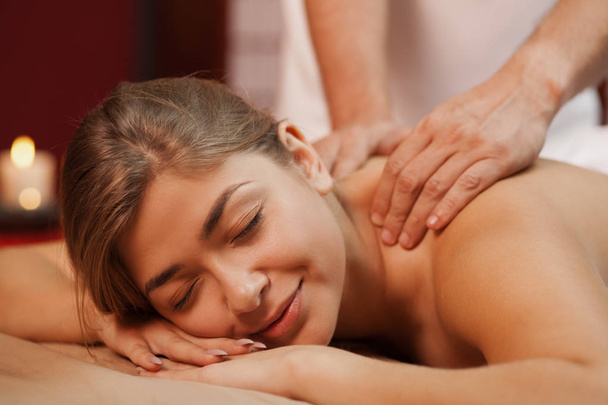 Close up of a happy woman smiling while receiving back massage. Professional masseur working at his beauty clinic, massaging back of his client. Female enjoying spa treatment. Happiness, relax concept - Foto, Imagem