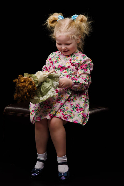 A little girl plays with a doll on a black background. - Photo, Image