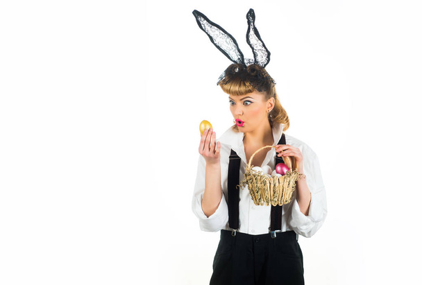 Egg surprise. Easter woman and golden egg. Holiday wish concept. Studio shot of a excited young woman wearing bunny ears and holding a of Easter eggs on white background. - 写真・画像