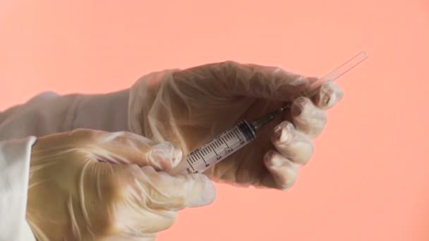 Doctor holding syringe and open needle on a pink background - Footage, Video