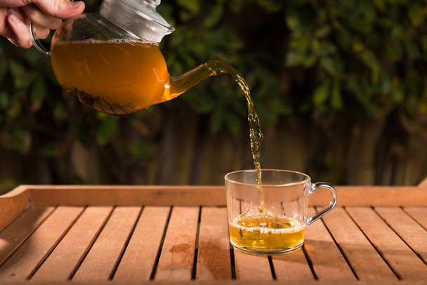 Pouring tea from a teapot into a cup on a blurred background of nature - Valokuva, kuva