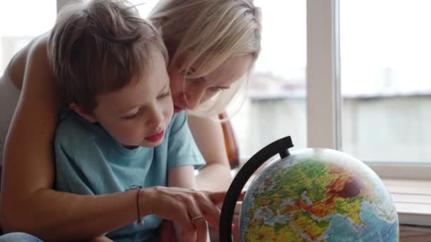 An attractive mother of caucasian ethnicity uses a globe to show her young son the countries of the world. - Metraje, vídeo