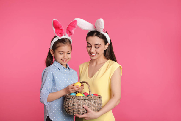 Mother and daughter in bunny ears headbands with Easter eggs on color background - Φωτογραφία, εικόνα