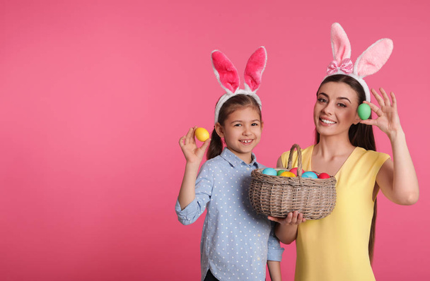 Mother and daughter in bunny ears headbands with Easter eggs on color background, space for text - Φωτογραφία, εικόνα