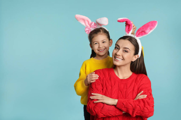 Mother and daughter in Easter bunny ears headbands on color background, space for text - Photo, image