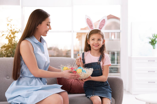 Mother and daughter holding basket with Easter eggs at home - Foto, afbeelding