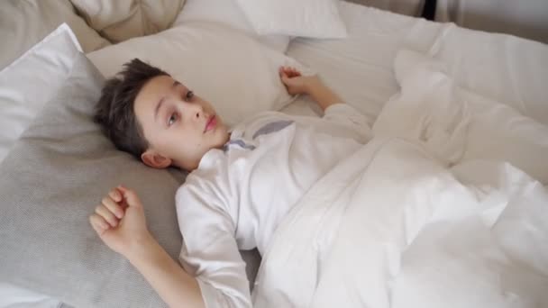 Cute teenager boy waking up in morning. Boy stretching in bed - Footage, Video