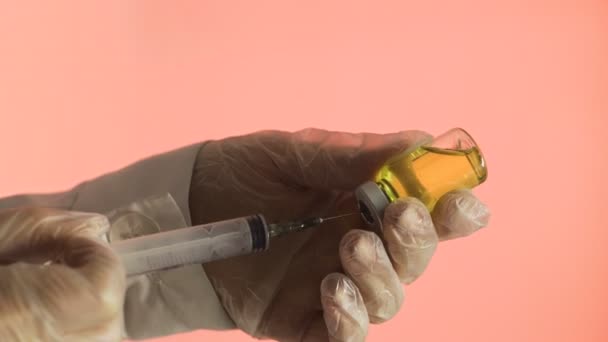 Plnění léku z ampule do injekční stříkačky žlutým lékem na růžovém pozadí - Záběry, video