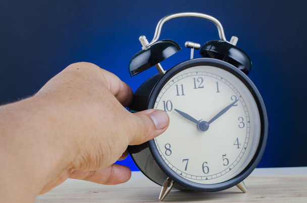hand holding alarm clock on wooden desk over dark background - Photo, Image
