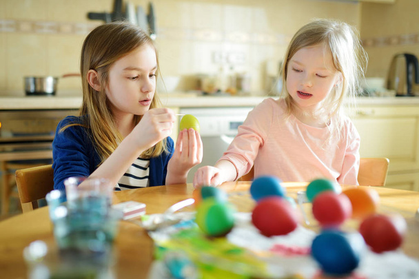Two cute young sisters dyeing Easter eggs at home. Children painting colorful eggs for Easter hunt. Kids getting ready for Easter celebration. Family traditions. - Fotografie, Obrázek