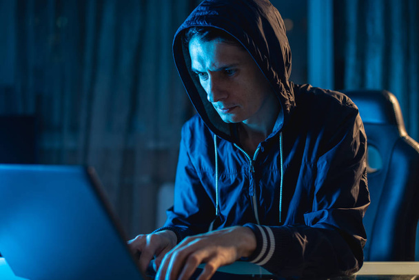 Cyberprzestępczy haker w kapturze wpisujący kod programu podczas kradzieży baz danych z hasłami. Bezpieczeństwo cybernetyczne - Zdjęcie, obraz