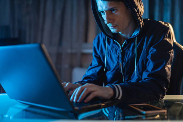 Хакер-киберпреступник в капюшоне печатает программный код, воруя базы данных доступа с паролями. Кибербезопасность - Фото, изображение