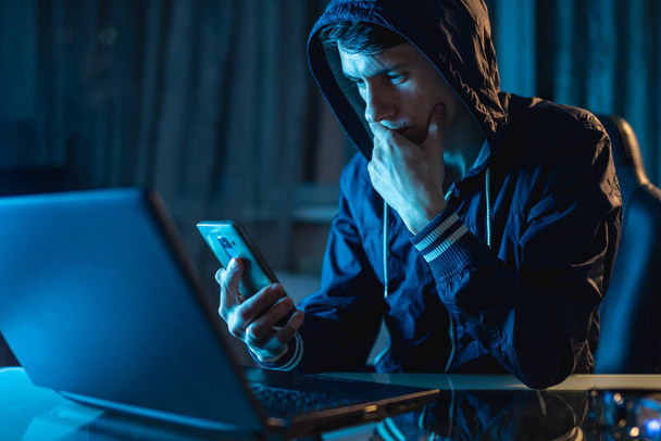 Hacker dans le capot tenant le téléphone dans ses mains en essayant de voler les bases de données d'accès avec des mots de passe. Cybersécurité
 - Photo, image