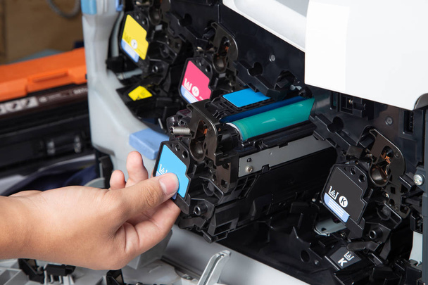 Zakenman of technicus controleert en verandert de cartridges van de printerapparatuur toon van laser jet multifunctionele printer in het kantoor. Close-up shot van Cmyk inktpatronen voor laserprinter. - Foto, afbeelding