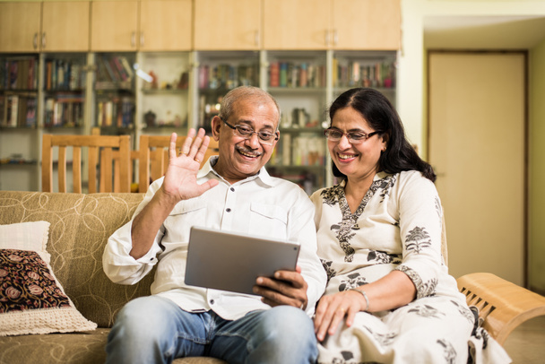 Indische/Aziatische Senior paar video chatten op tablet/computer zittend op de Bank of in tuin thuis, selectieve aandacht - Foto, afbeelding