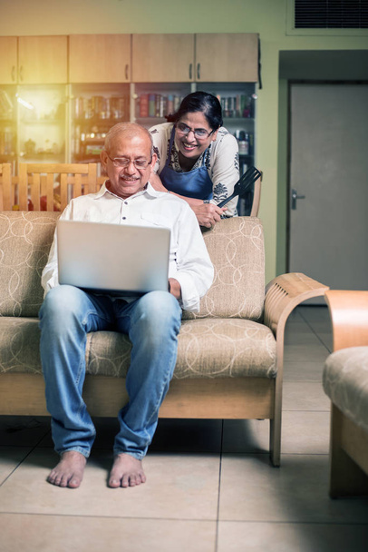 Senior Indian/asian couple accounting, doing home finance and checking bills with laptop, calculator and money while sitting at home garden - Zdjęcie, obraz